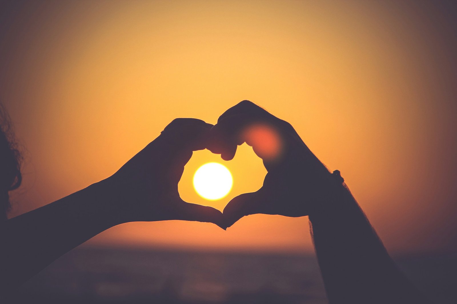 Two hands forming a heart shape around the sun at sunset