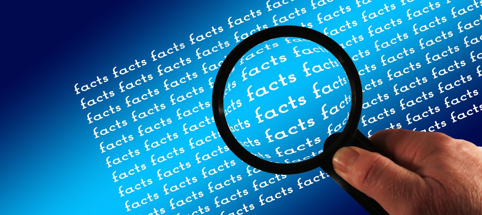 A hand holding a magnifying glass over a background of the repeated word “facts”